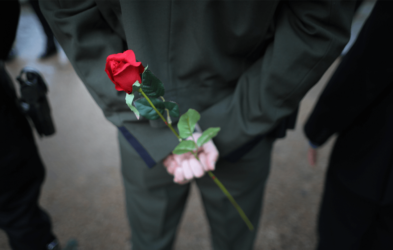 Three law enforcement officers stand next to one another with hands clasped behind their backs. One is holding a single rose.