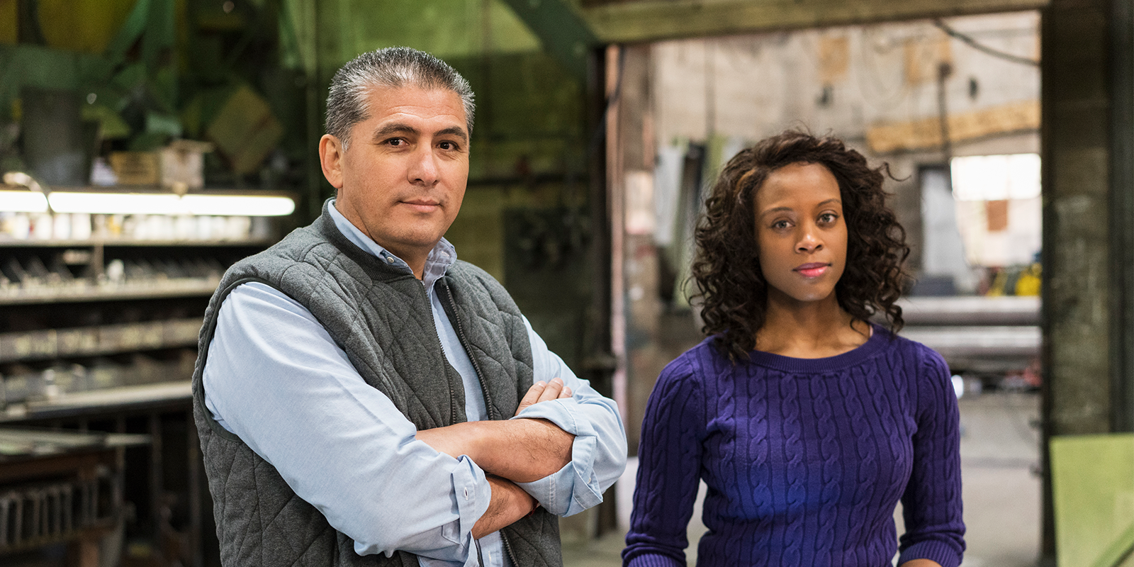 Photo of a man with his arms crossed standing next to a woman with curly hair.